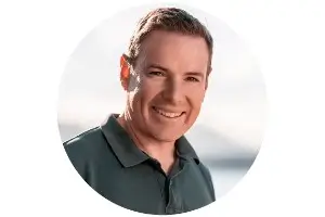 Circular headshot of a smiling man wearing a dark polo shirt against a bright, softly lit background.