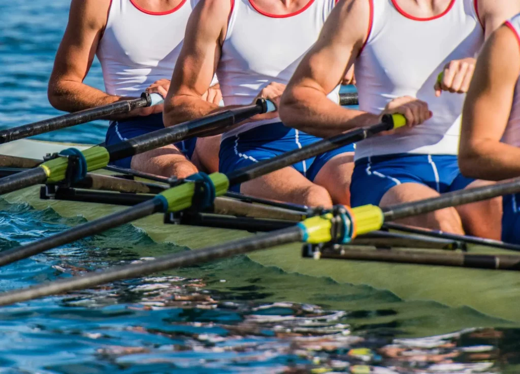 A close-up view of a rowing crew in matching white and blue uniforms rowing in perfect synchronization on the water.